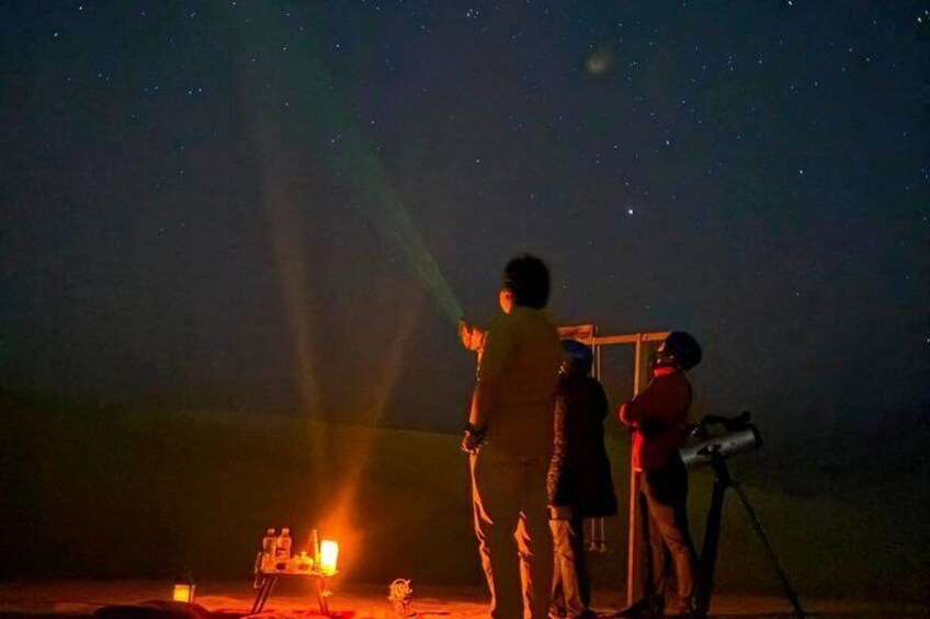 A group of people observing the night sky with a telescope and a light source. 1