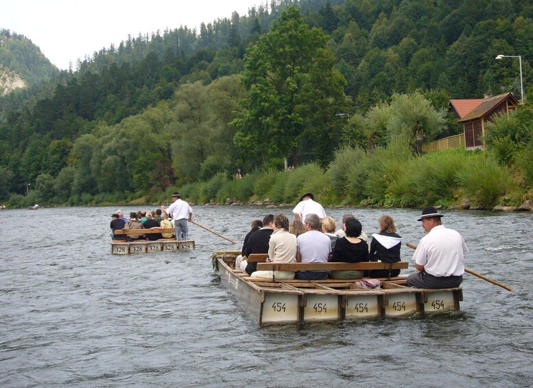 A group of people rowing in wooden boats on a river, surrounded by dense forest and a small building on the bank. 5