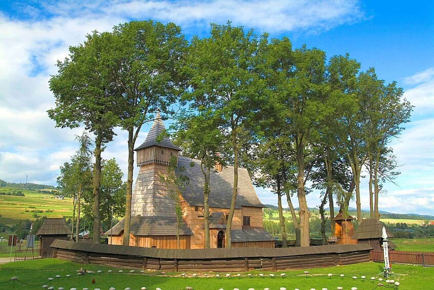 A historic wooden building surrounded by trees and a fenced area with sheep. 2