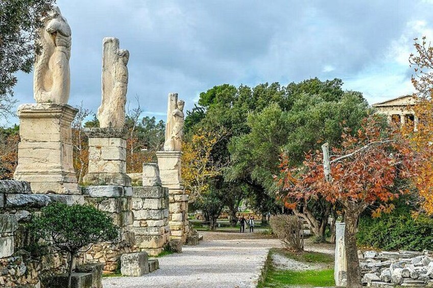 Ancient ruins with stone statues, a pathway, and a classical building in the background. 4