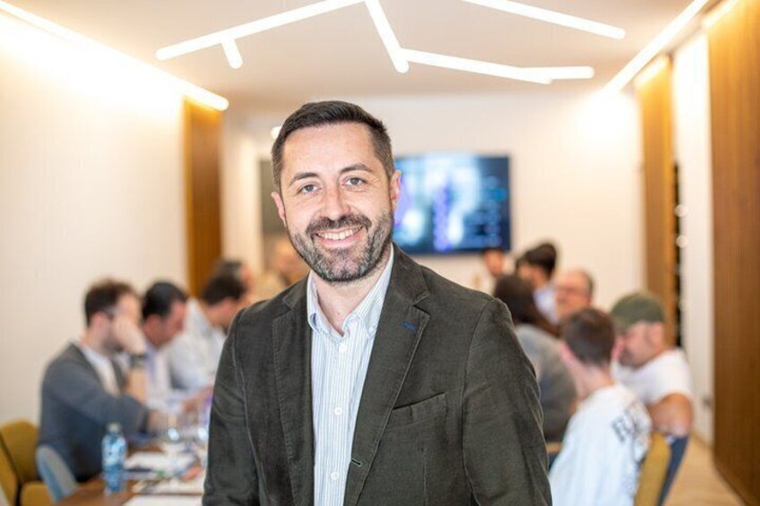 A man in a suit standing in a conference room with a television screen in the background. 1