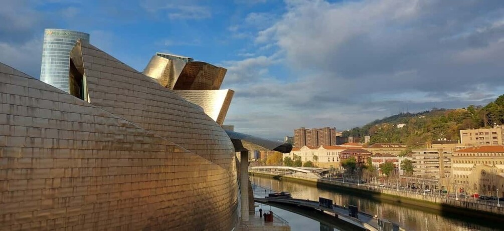A modern architectural structure with a curved metallic facade, a river, and surrounding urban buildings. 2