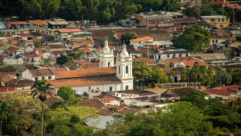 A densely packed urban area with a prominent white church featuring a bell tower, surrounded by residential buildings with red-tiled roofs and lush greenery. 1