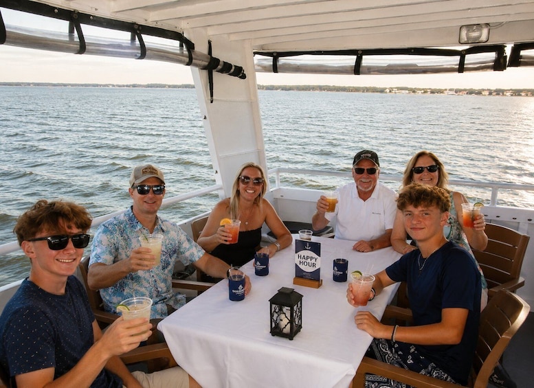 A group of people on a boat with drinks, a table with a 'Happy Hour' sign, and a view of the water. 4