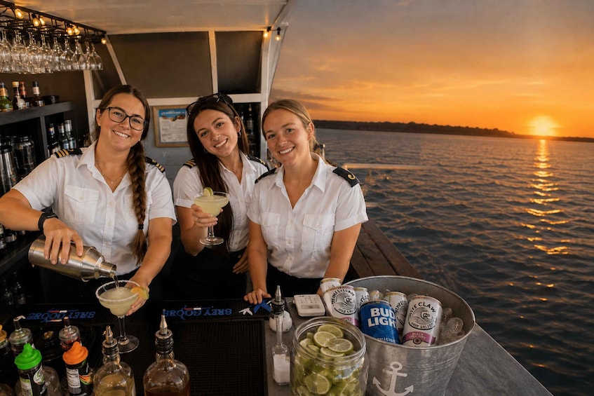Three bartenders on a boat at sunset, with drinks and bottles on the bar. 2