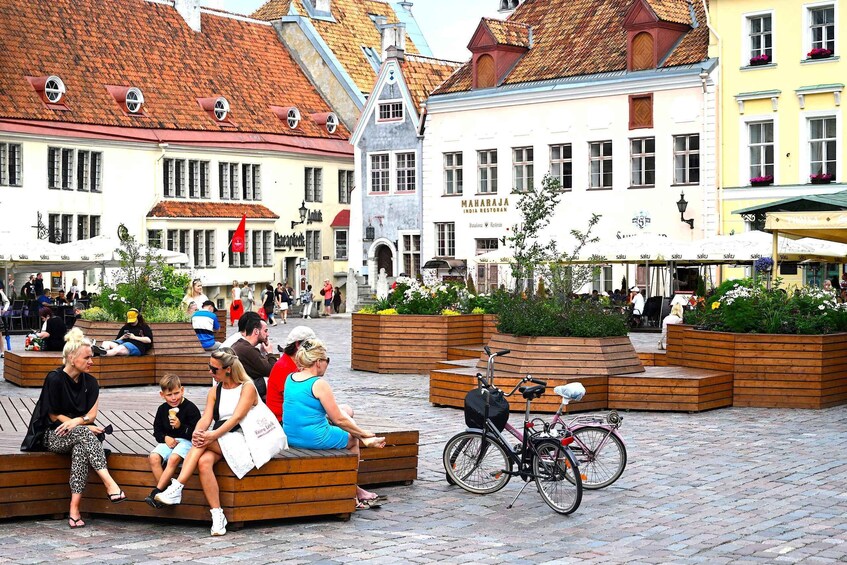 A bustling European square with wooden benches, a bicycle, and historic buildings with red-tiled roofs. 3