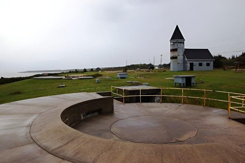 A coastal landscape with a church, a circular concrete structure, and a grassy field. 1
