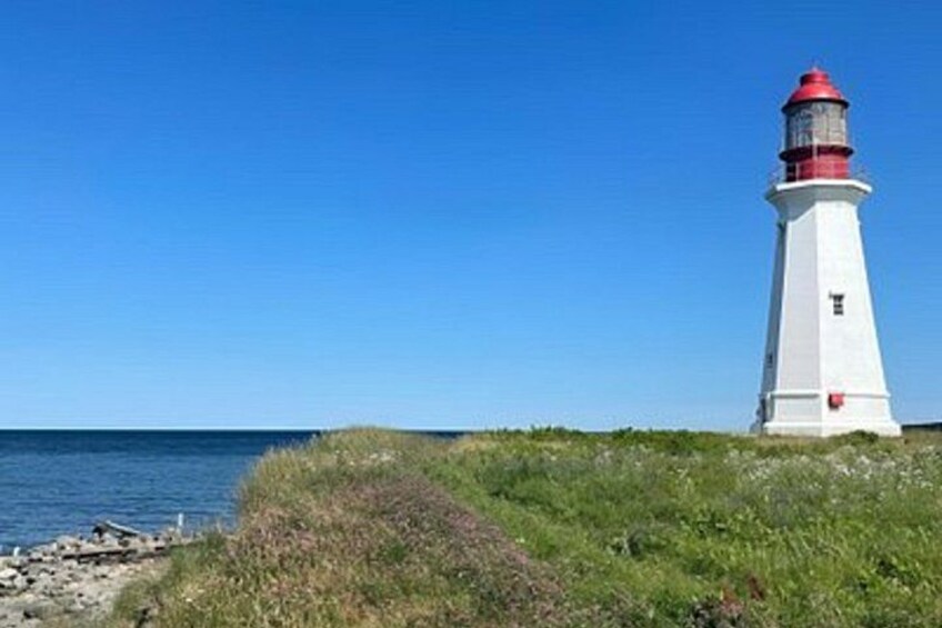 A white lighthouse with a red top, situated on a grassy cliff by the sea. 4
