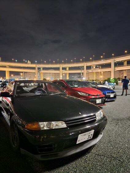 A nighttime parking lot with multiple cars, a bridge in the background, and streetlights. 3