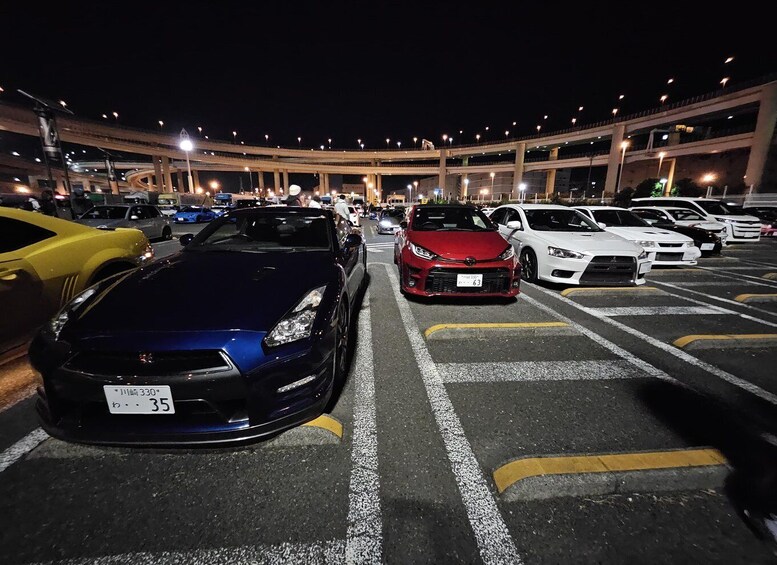 A parking lot with cars, including a blue sports car and a red sports car, under a covered structure with lights. 1
