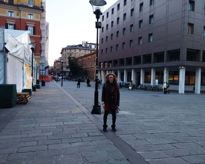 A person standing on a paved street with buildings and parked bicycles in the background. 3