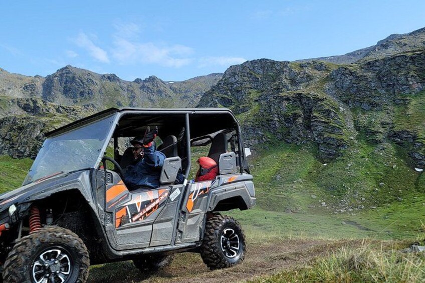 A four-wheeled vehicle with a roof, parked on a grassy hillside with mountains in the background. 1