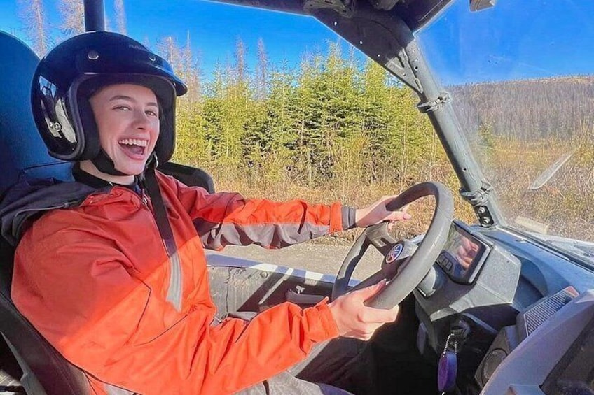 A person in a red jacket driving a vehicle with a steering wheel and dashboard. 3
