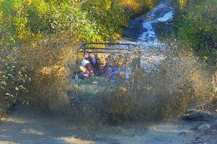 A vehicle navigating through a narrow, muddy path surrounded by dense vegetation. 2
