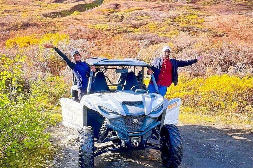 A white off-road vehicle on a dirt path with two people standing beside it. 4