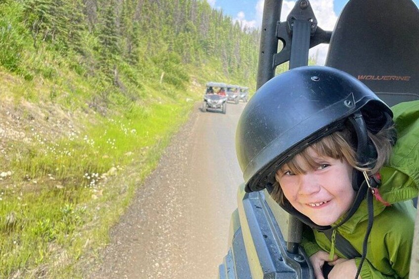 A person in a green jacket and helmet on a vehicle, a dirt road, and a forested area. 4