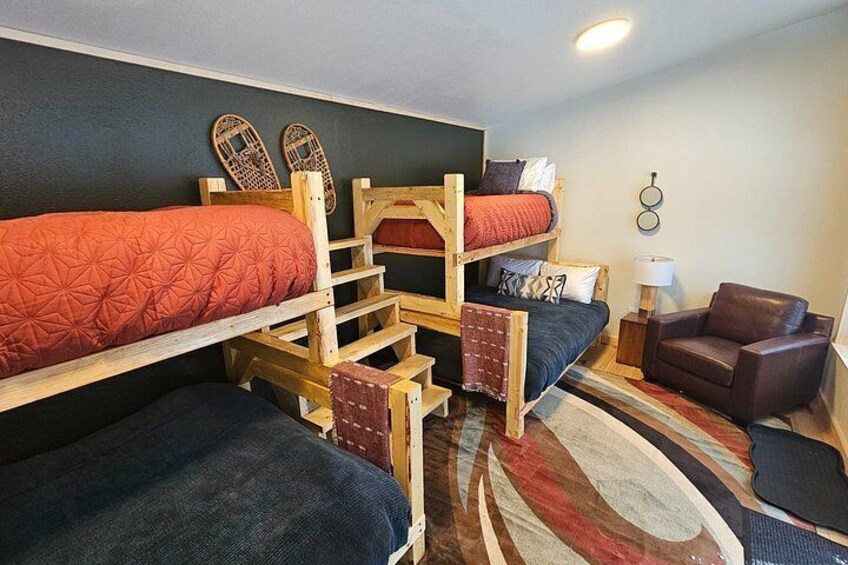 A bunk bed room with a wooden ladder, a brown leather chair, and a patterned rug. 5