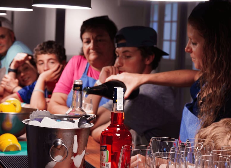 A group of people at a social gathering with a bottle of red liquor and glasses on a table. 4