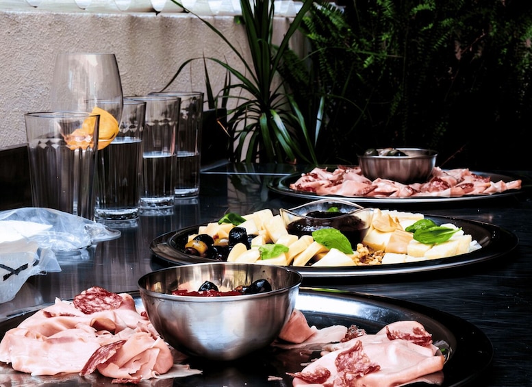A table with plates of cured meats, olives, cheese, and a bowl of olives and nuts. 2
