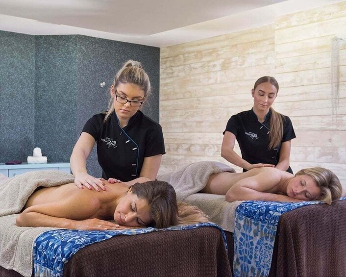 A massage therapy session in a spa with two therapists attending to clients on massage tables. 3