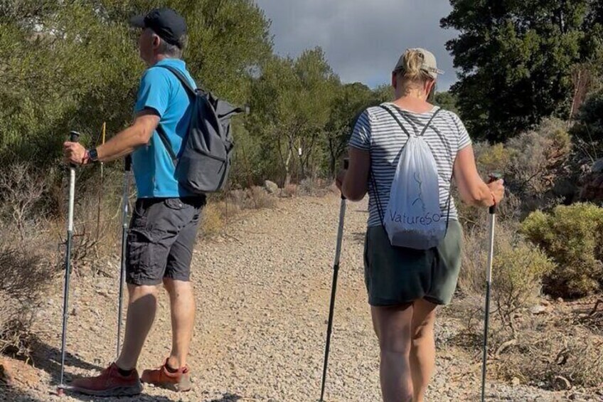 Two people hiking on a gravel path with trees and shrubs in the background. 2