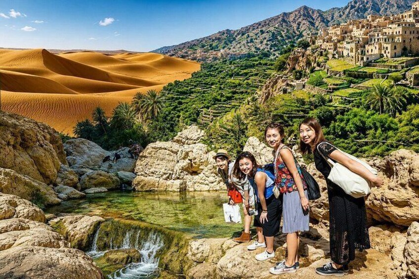 A group of people standing by a water stream with sand dunes and terraced fields in the background. 1