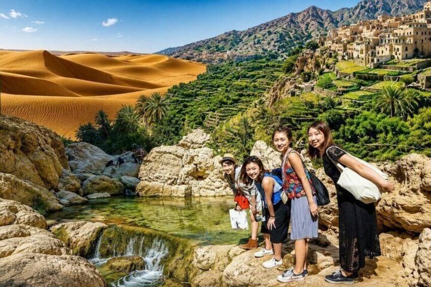 A group of people standing by a water feature with sand dunes and terraced fields in the background. 1
