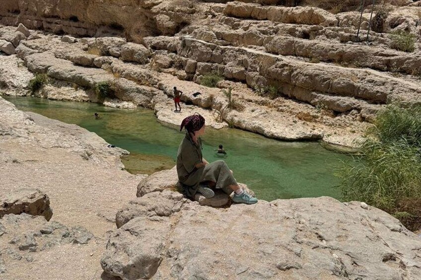 A person sitting on a rock by a clear water body surrounded by rocky terrain. 2