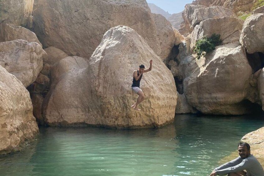 A person jumping off a rock into a body of water surrounded by large boulders. 4