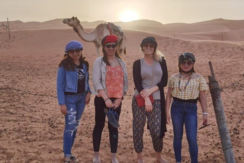 Four people standing in a desert with a camel in the background. 3
