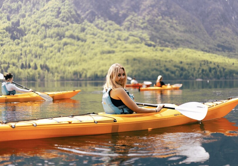 A person kayaking on a calm lake with forested hills in the background. 1