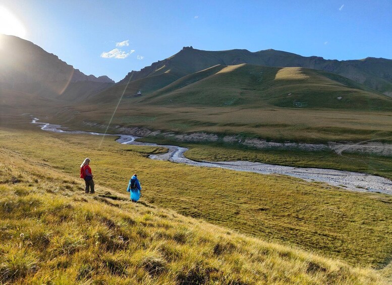 A mountainous landscape with a river, two hikers, and a clear sky. 3