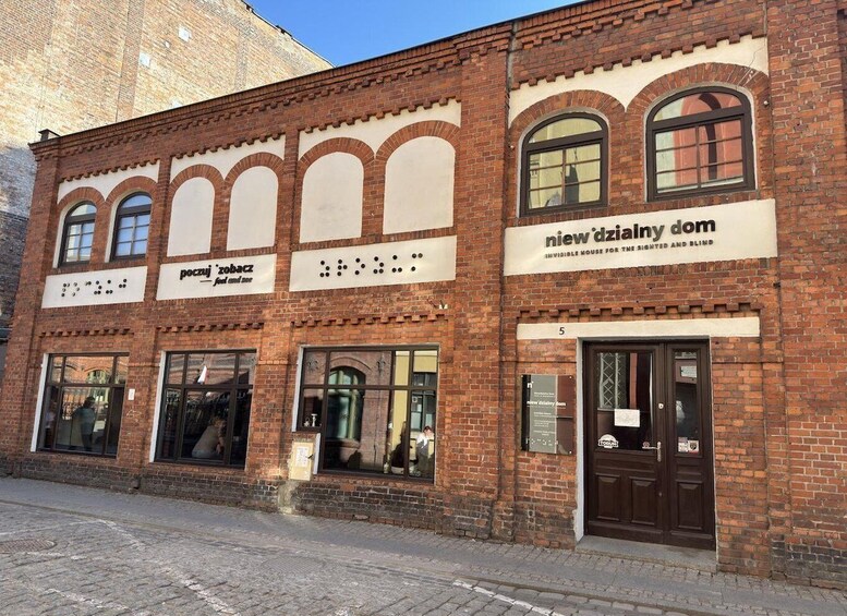 A brick building with arched windows and signs for 'poczuj zobacz' and 'new dzialny dom.' 1