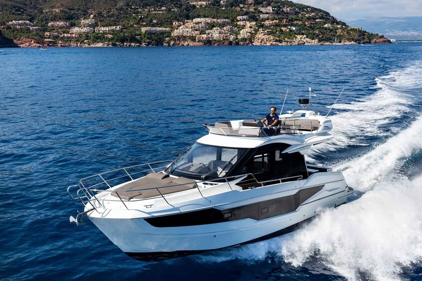 A white speedboat with a single person on deck, moving through a body of water with a coastal town in the background. 2