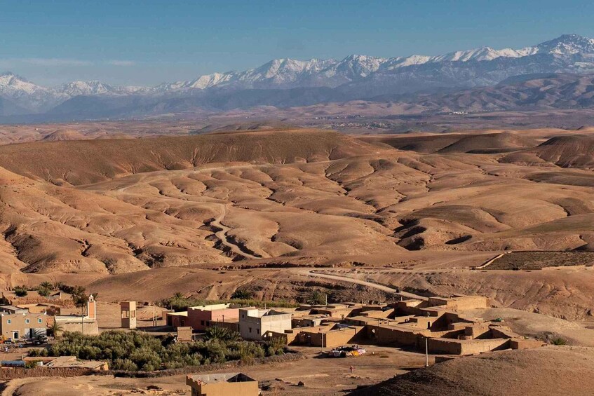 A desert landscape with undulating hills and a small settlement with traditional buildings. 1