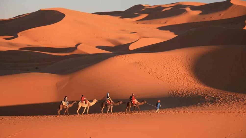 A group of people riding camels across a desert landscape with sand dunes. 2