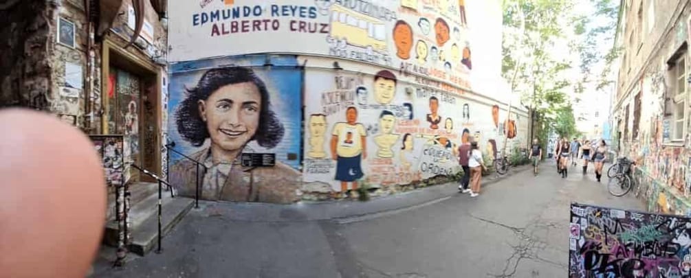 A narrow street with a mural featuring portraits and text, bicycles, and pedestrians. 5