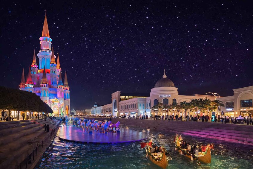 A nighttime cityscape with a brightly lit castle, a domed building, and a water fountain. 2