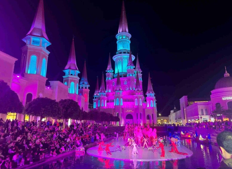 A castle with multiple spires, illuminated in pink and blue lights, surrounded by a crowd of people. 4
