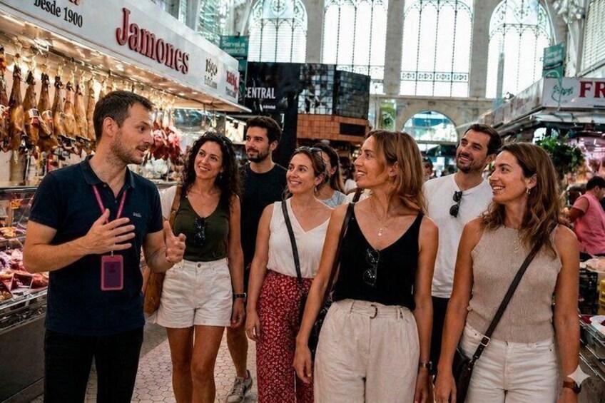A group of people in a market with a sign reading 'Jamones desde 1900'. 1