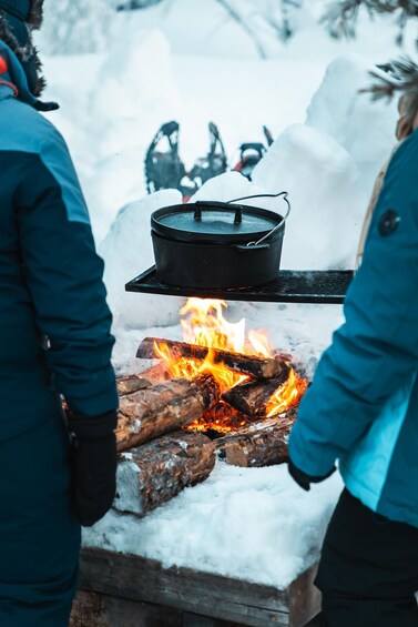 A person cooking over an open fire with a pot on a stand, surrounded by snow. 1