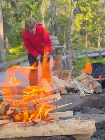 A person in a red jacket tending a campfire with logs and flames. 4
