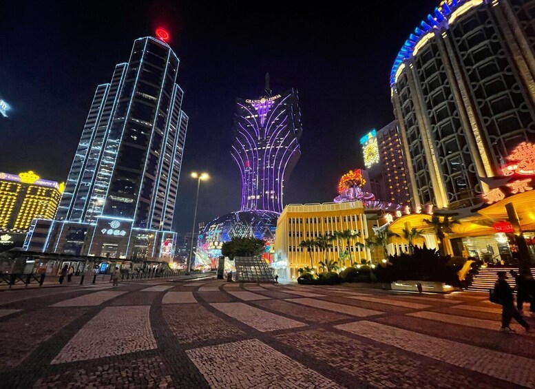 A nighttime cityscape with illuminated buildings, including a prominent tower with a unique design. 1