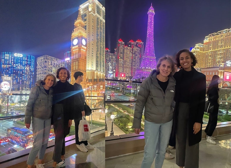 A group of people standing on a balcony overlooking a cityscape with illuminated landmarks, including a clock tower and a tall tower with purple lights. 2