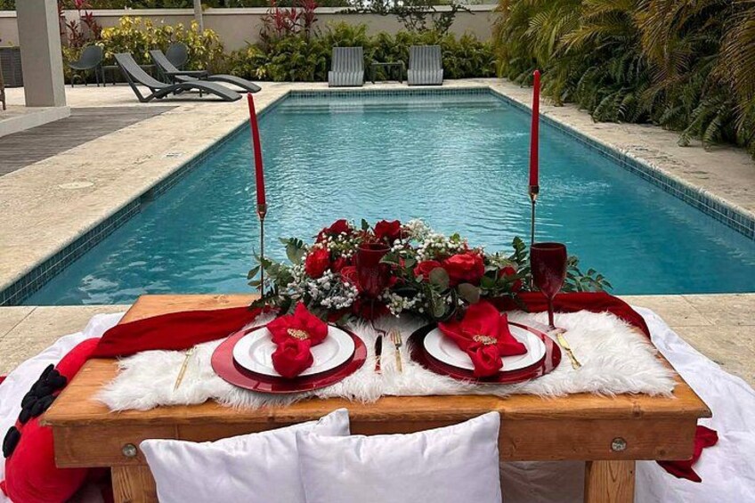 A poolside dining setup with a table, red and white plates, and a floral centerpiece. 3