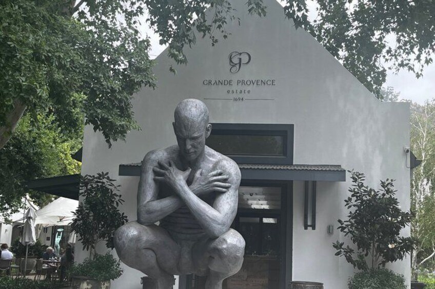 A statue of a man in a crouched position in front of a building with 'GRANDE PROVENCE' signage. 5