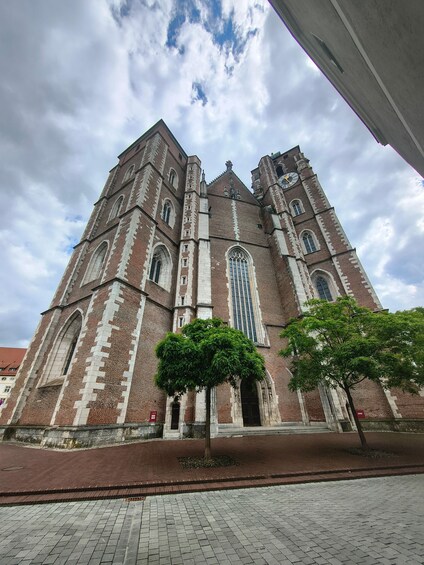 A large brick church with a clock tower, arched windows, and a red brick pathway in front. 1