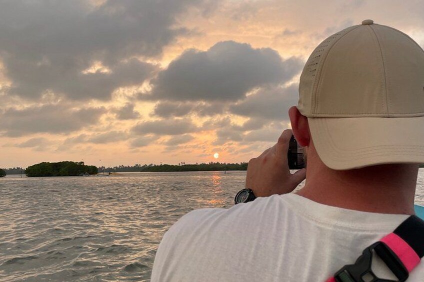 A person taking a photo of the sunset over a body of water with an island in the distance. 3