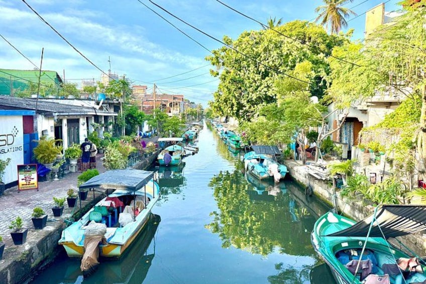 A narrow waterway lined with boats, buildings, and greenery. 1