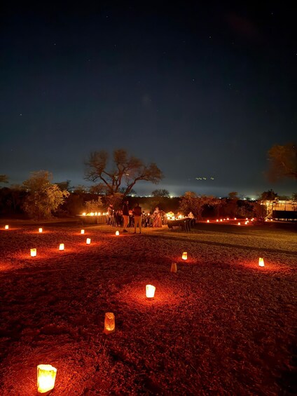 A nighttime outdoor event with people gathered around tables, lit by candles on the ground. 2